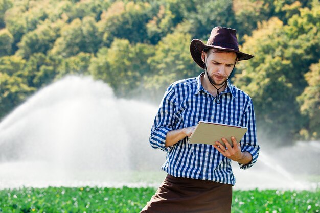 O engenheiro agrônomo verifica a colheita e usa a tecnologia do computador na plantação com sistema de aspersão.