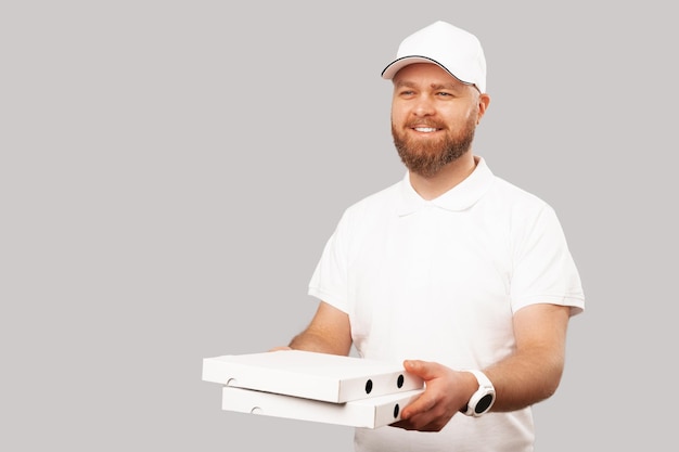 O entregador barbudo sorridente vestindo branco segura algumas caixas de almoço ou pizza