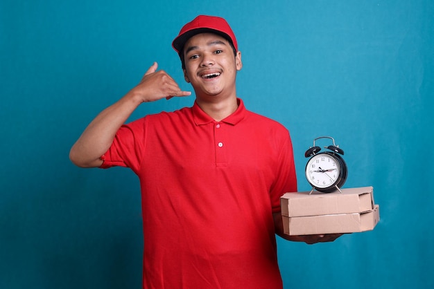 O entregador de uniforme vermelho está segurando caixas de pizza e um relógio enquanto faz o gesto de chamada. em ti