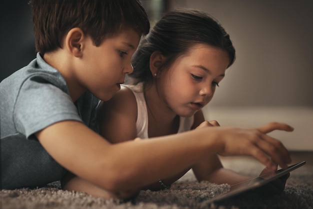 O entretenimento para crianças está a apenas um aplicativo de distância foto de um adorável irmão e irmã usando um tablet digital juntos no chão em casa