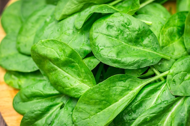 O espinafre suculento fresco sae em uma tabela marrom de madeira. Produtos naturais, verduras, alimentos saudáveis