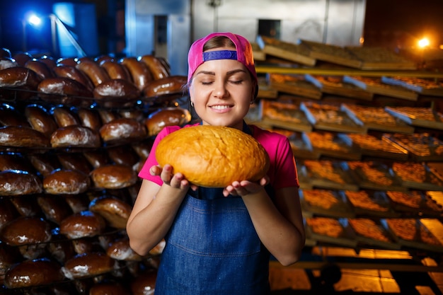 O estágio de cozimento em uma padaria. Retrato de uma menina padeiro com pão nas mãos no contexto das prateleiras em uma padaria. Mãos de um padeiro com pão. Produção de pão industrial