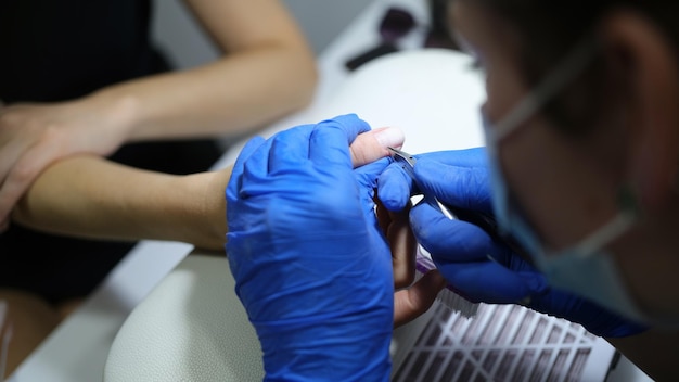 O esteticista apara as cutículas das unhas dos clientes no processo de manicura do salão closeup conceito de cuidado corporal