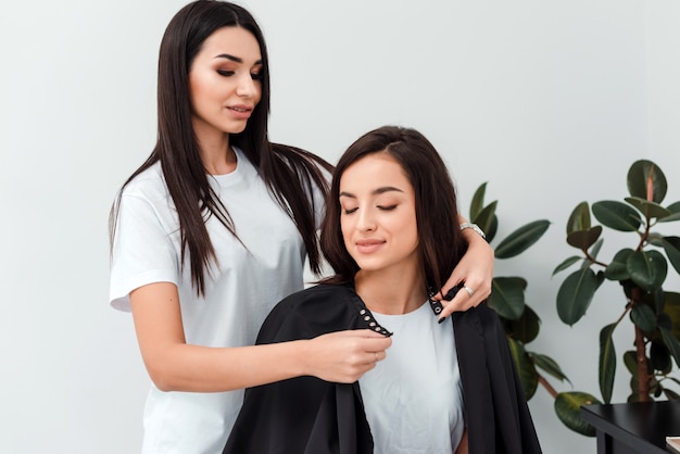 O estilista atrativo da menina veste o vestido do cabeleireiro do cliente