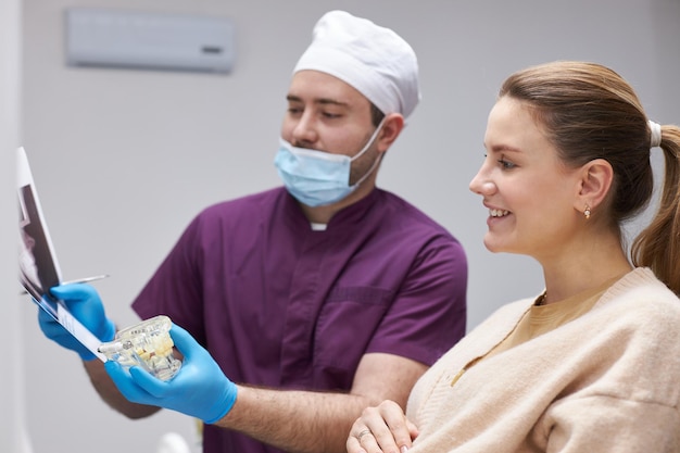 O estomatologista segura o filme dental panorâmico de raios X e um modelo plástico da mandíbula humana durante a consulta