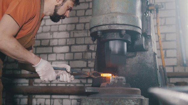 O ferreiro forja o metal no martelo mecânico - um pequeno negócio,