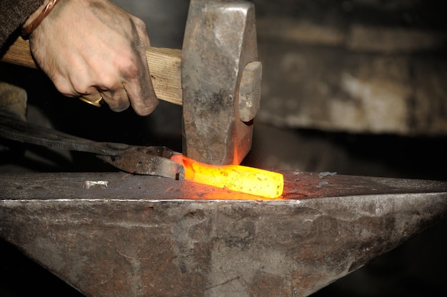 O ferreiro que trabalha na forja processa o metal A fotografia sobre o tema da ferraria