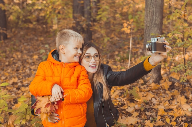 O filho e a mãe estão tirando uma selfie para a câmera no parque de outono, lazer para pais solteiros e no outono