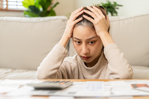 O financeiro deve a jovem asiática sentada sofrer estressado e confuso por calcular despesas de fatura ou conta não tem dinheiro para pagar hipoteca ou empréstimo Falência de dívida ou conceito de falência