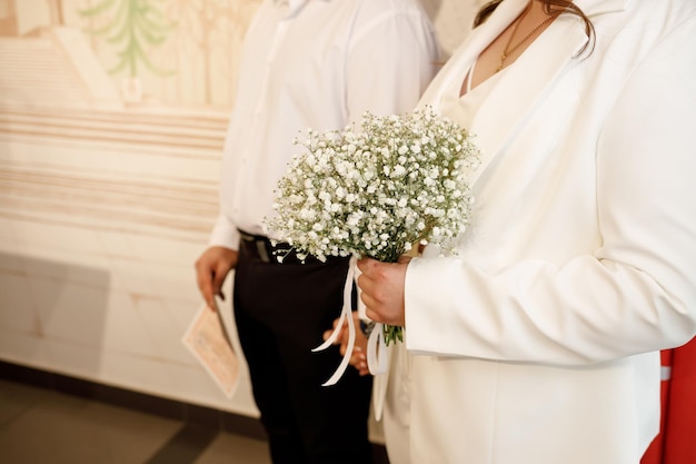 O foco está no buquê branco da noiva que ela está segurando nas mãos