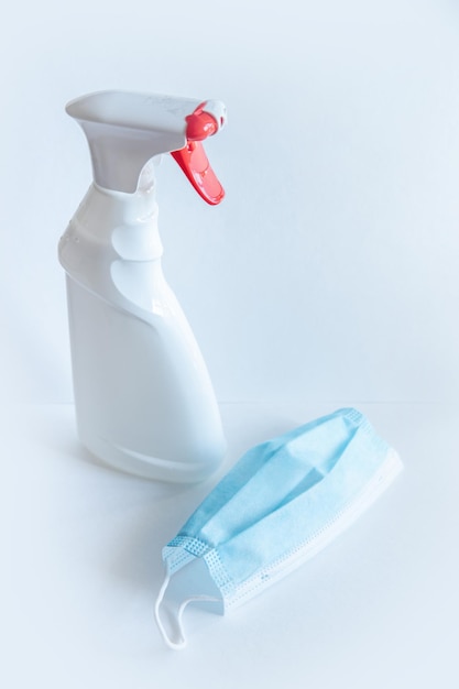 O frasco spray de cor branca com o botão vermelho um sabonete líquido e máscara médica está sobre uma mesa