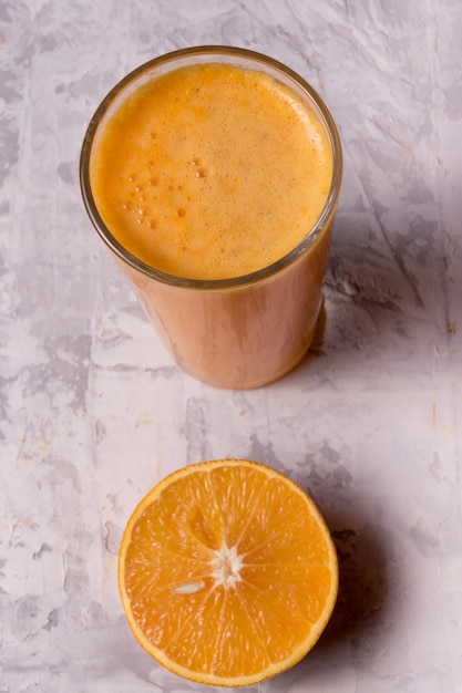 Foto o fruto maduro da tangerina cortou ao meio e ao suco de laranja em um vidro, sobre o fundo branco rústico.