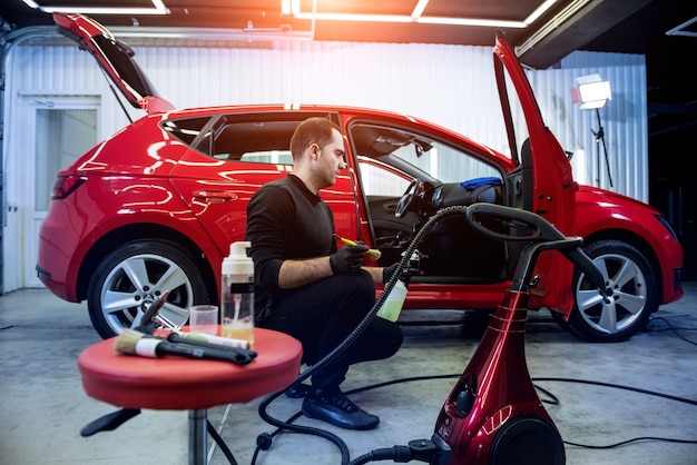 O funcionário da manutenção de automóveis limpa o interior com uma escova especial