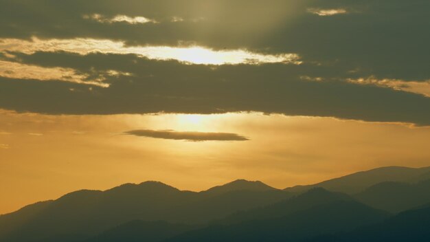 O fundo do nascer do sol sobre as montanhas, a silhueta e as nuvens em tempo real