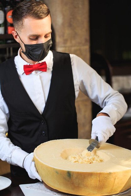 O garçom corta pedaços de queijo parmesão