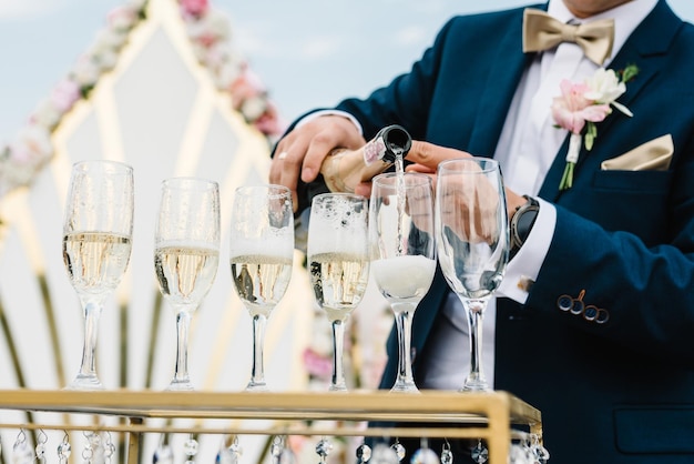 O garçom derrama o champanhe nos copos da garrafa na festa evento oficial do banquete do serviço de catering