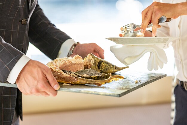 O garçom mãos corte esturjão cozido no restaurante