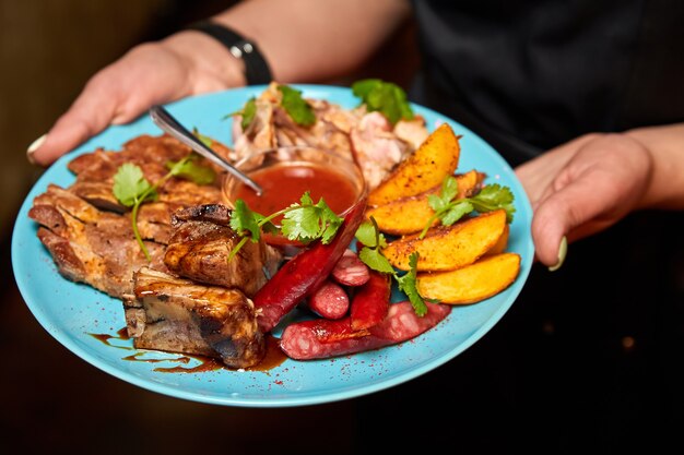 O garçom segura um prato de carne com batatas assadas e molho de tomate