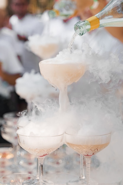 O garçom serve champanhe em taças de cristal com gelo seco e fumaça branca de perto