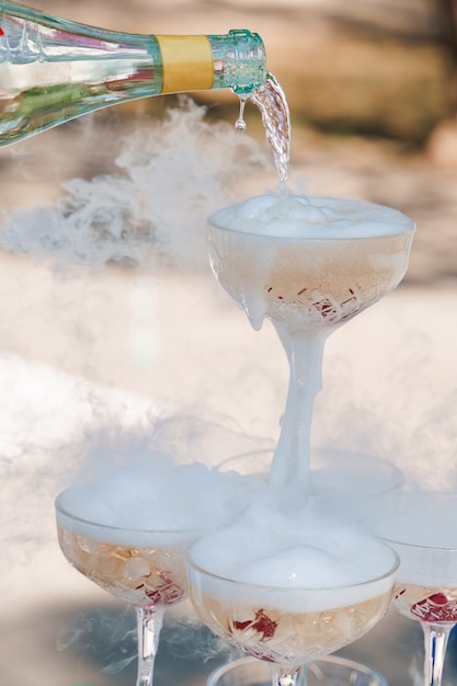 O garçom serve champanhe em taças de cristal com gelo seco e fumaça branca de perto