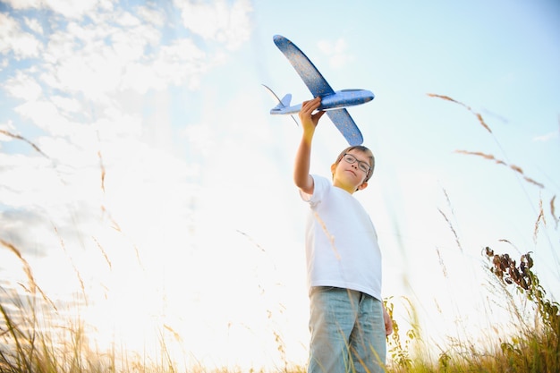 O garoto corre com um avião de brinquedo filho sonha em voar menino feliz corre no sol brincando com um avião de brinquedo no campo de verão