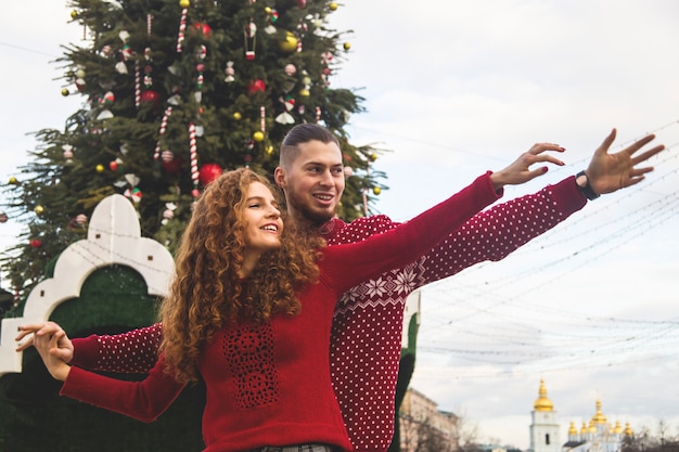 O garoto e a garota de camisola vermelha estão sorrindo alegremente para a árvore de Natal.