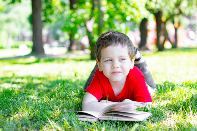 O garoto está deitado na grama e lendo um livro. Leitura na natureza.