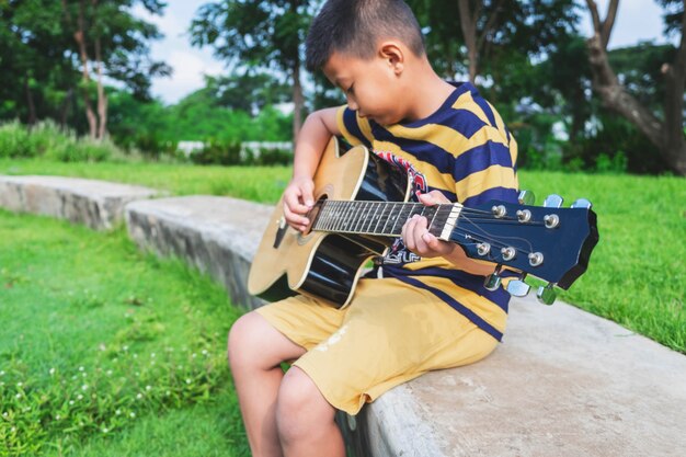 O garoto está tocando violão no jardim.