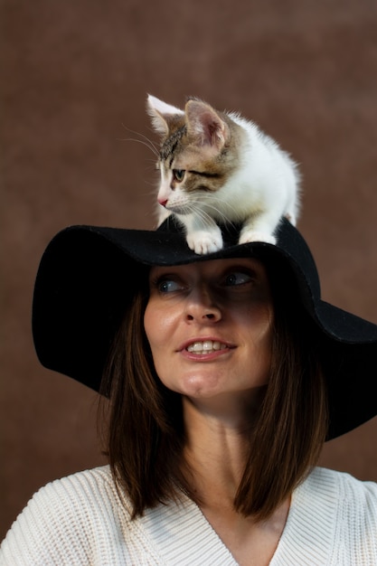 O gatinho branco está sentado no chapéu com uma grande cabeça de aba de uma jovem