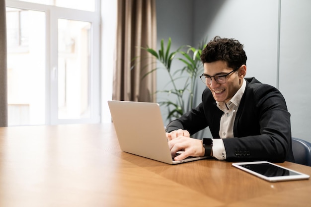 O gerente de óculos trabalha no escritório usa um laptop faz um relatório on-line