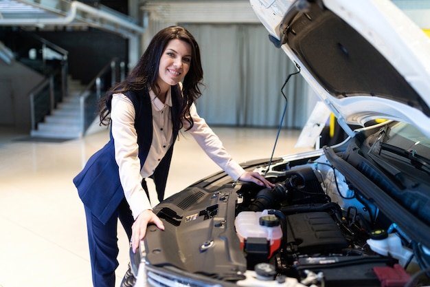 O gerente de venda bonito inspeciona o carro novo no showroom da concessionária