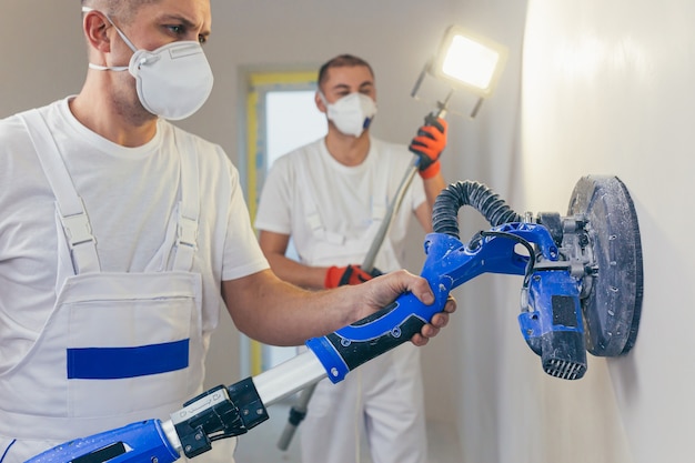 O gesso alisa a superfície da parede com uma máquina de parede com lixa.