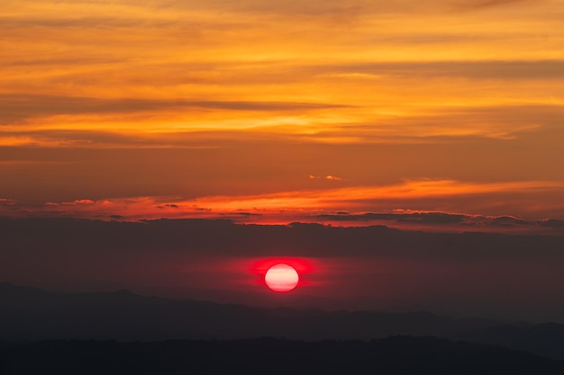 O grande sol nascente vermelho está prestes a se pôr em meio ao céu laranja dourado