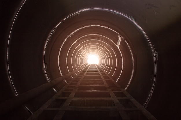 O grande tubo de aço do túnel tem sombra e luz pretas no final do túnel.