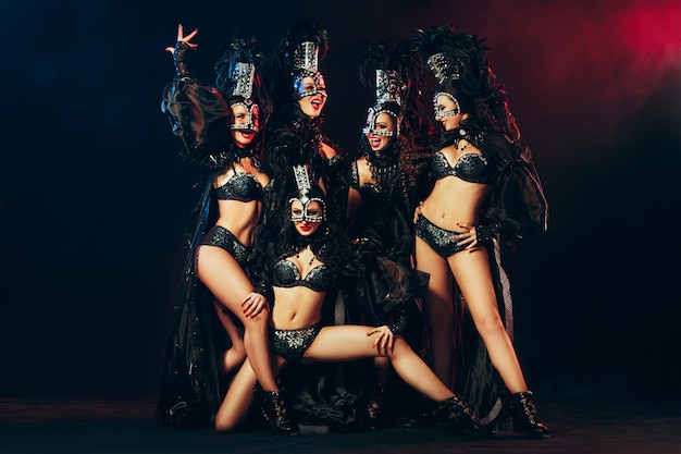 O grupo de jovens felizes e sorridentes lindas dançarinas com vestidos de carnaval posando em fundo preto do estúdio