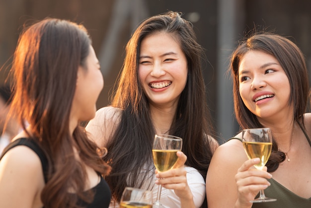 O grupo de mulheres asiáticas felizes bonitas novas que guardam o vidro do vinho conversa junto com os amigos ao comemorar o dance party no clube noturno exterior do telhado, estilo de vida do lazer do conceito novo da amizade.