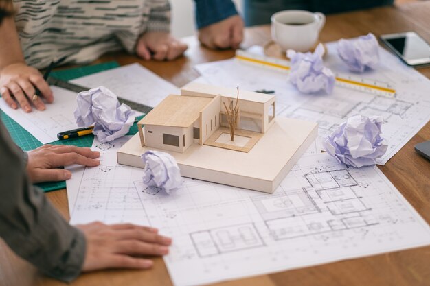 O grupo de um arquiteto sente-se estressado depois de trabalhar no modelo de arquitetura junto com o papel de desenho da loja na mesa do escritório