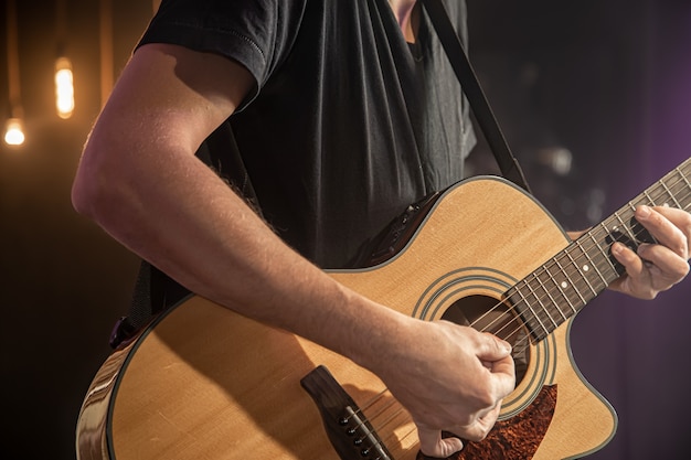 O guitarrista toca violão em show com uma palheta em um fundo preto desfocado close-up.