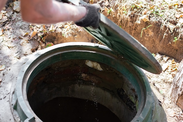 Foto o homem abre uma escotilha de esgoto. inspeção e manutenção de fossas sépticas.