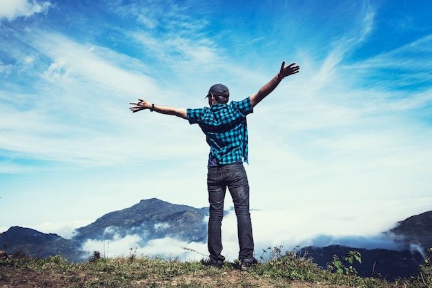 O homem abriu os braços para os lados contra o céu azul nublado e os picos das altas montanhas. Cena emocional. Conceito de vitória de aventura e negócios de viagens de liberdade. Vento forte nas montanhas. mãos ao ar