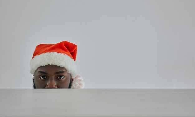 O homem africano com chapéu de Papai Noel olhando da mesa