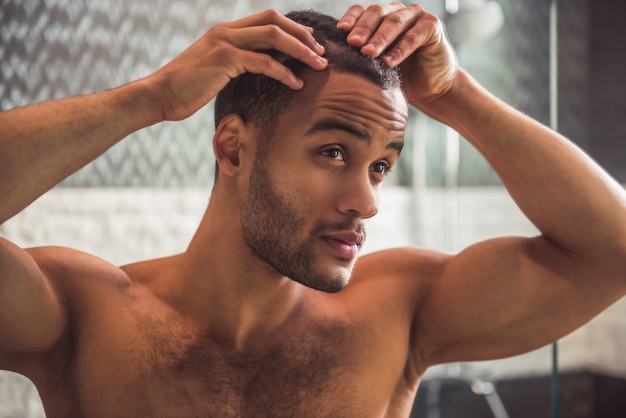 O homem afro-americano despido considerável está examinando seu cabelo.