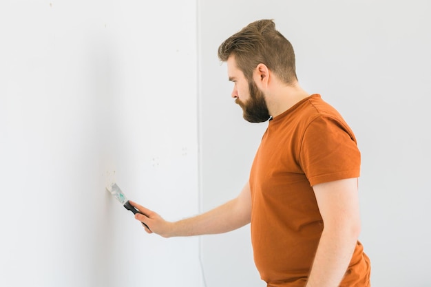 O homem alisa a superfície da parede com um moedor de parede, moendo uma parede de gesso branco, renovando e redecorando