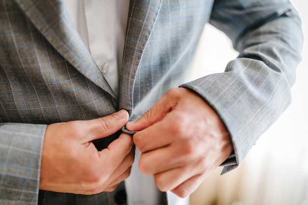 O homem aperta os botões. O noivo de terno, camisa está de pé no fundo branco. Fechar-se.