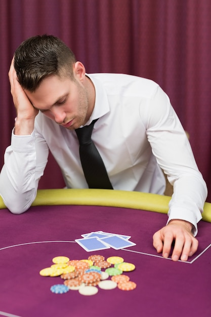 O homem apoiado na mesa de poker parece desapontado