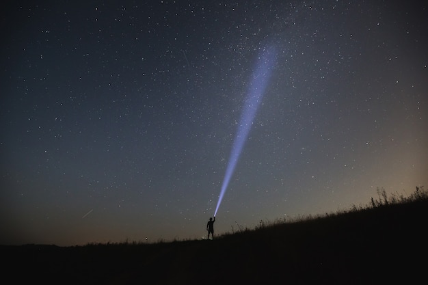 O homem aponta a lanterna para o céu noturno. noite de verão.