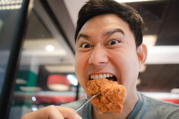 O homem asiático da cara engraçada come o frango frito.