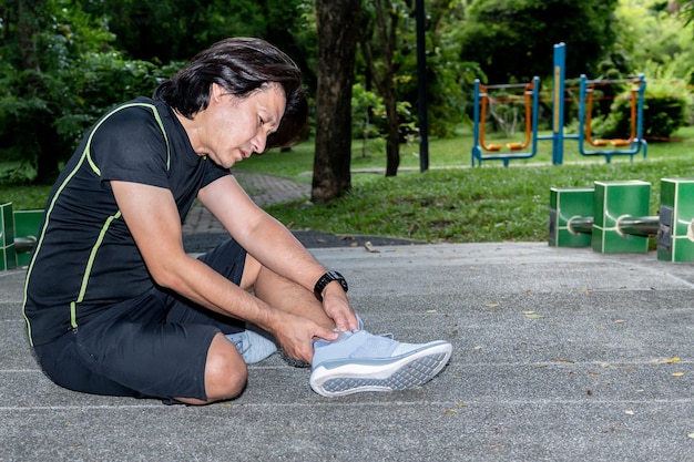 O homem asiático está atualmente tendo uma lesão no tornozelo durante seu exercício correndo na corrida