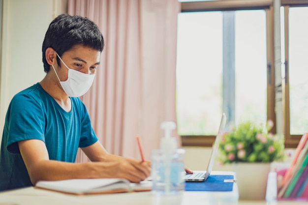 Foto o homem asiático está trabalhando em casa durante o coronavirus ou o covid-19. usando uma máscara facial para proteger contra o coronavírus.