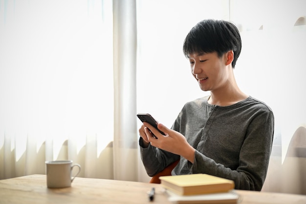 O homem asiático feliz gosta de conversar com seus amigos ou navegar nas mídias sociais no telefone